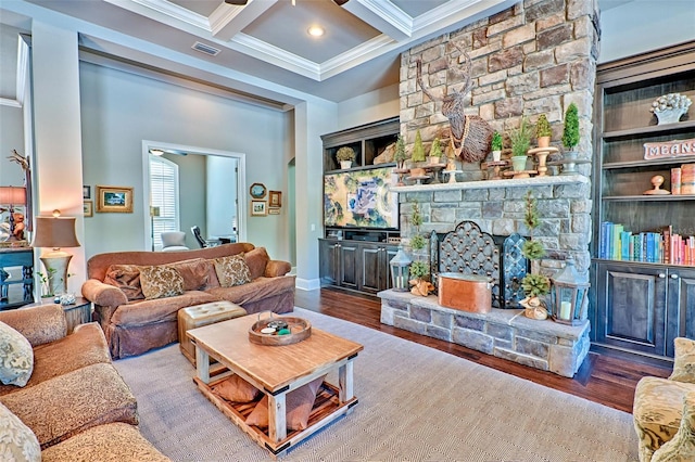 living room with coffered ceiling, beamed ceiling, wood finished floors, crown molding, and a stone fireplace