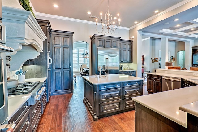 kitchen featuring arched walkways, a center island with sink, stainless steel appliances, light countertops, and dark wood-type flooring