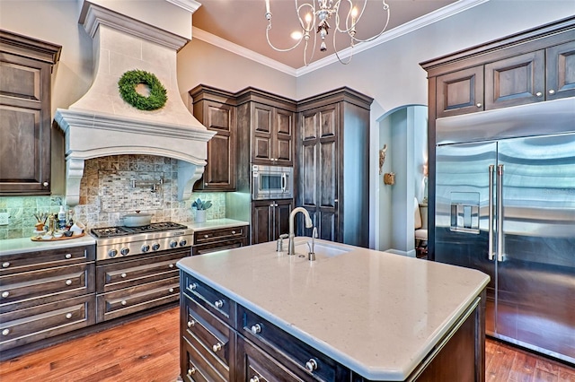 kitchen with arched walkways, tasteful backsplash, ornamental molding, a sink, and built in appliances