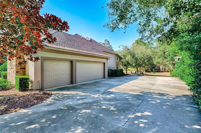 view of side of home featuring a garage, concrete driveway, a shingled roof, and stucco siding