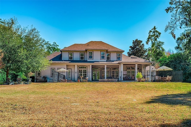 rear view of property featuring stucco siding, fence, and a yard