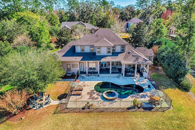 rear view of house with a yard, a patio, an in ground hot tub, a fenced backyard, and a fire pit