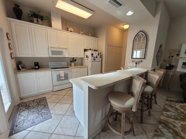 kitchen featuring light countertops, visible vents, white appliances, a peninsula, and a kitchen bar