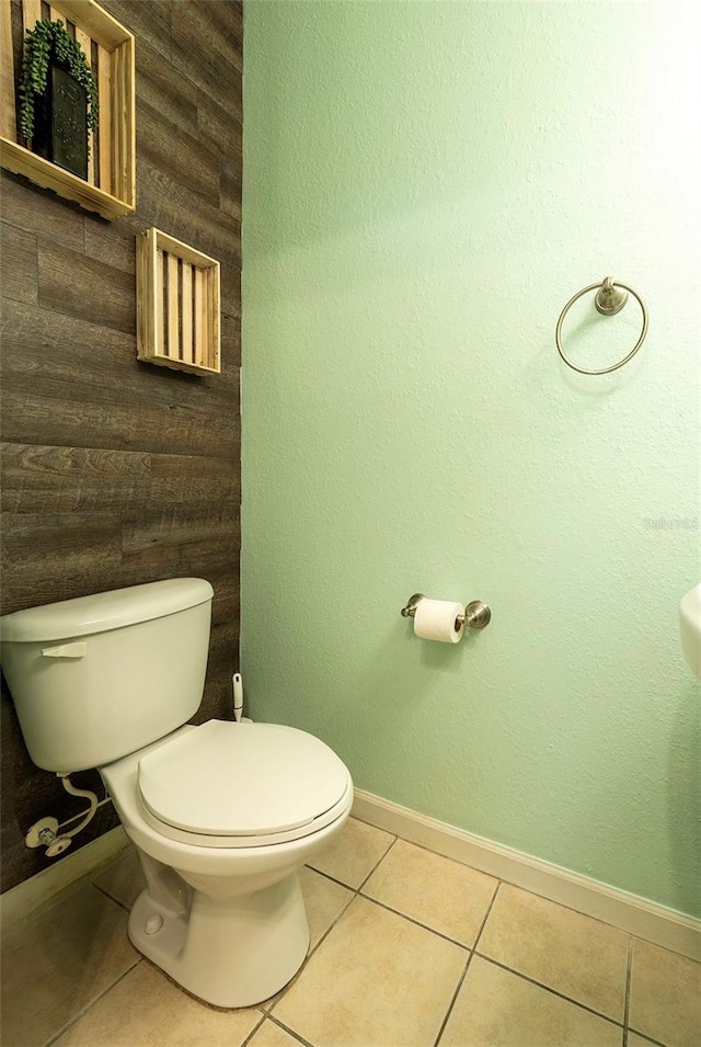 half bath featuring baseboards, toilet, and tile patterned floors