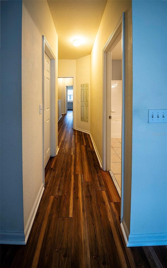 corridor with dark wood-type flooring and baseboards