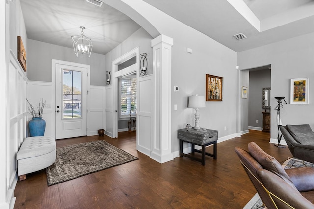 entrance foyer featuring visible vents, dark wood-style floors, arched walkways, a decorative wall, and ornate columns