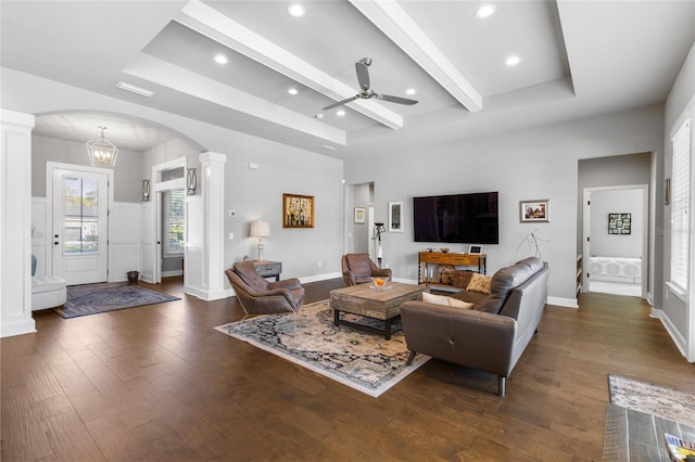 living area featuring arched walkways, ornate columns, a tray ceiling, and dark wood-style flooring