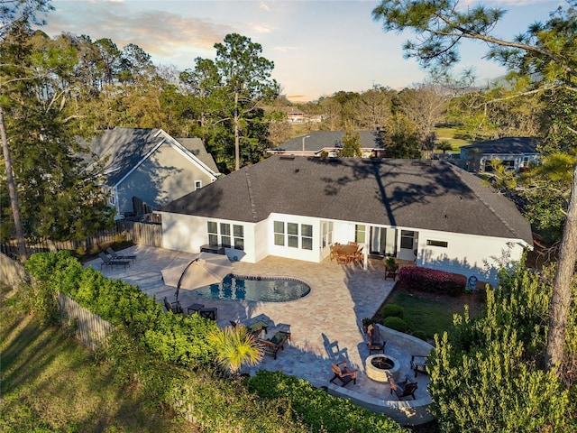 back of house at dusk with a fenced backyard, stucco siding, a fire pit, and a patio