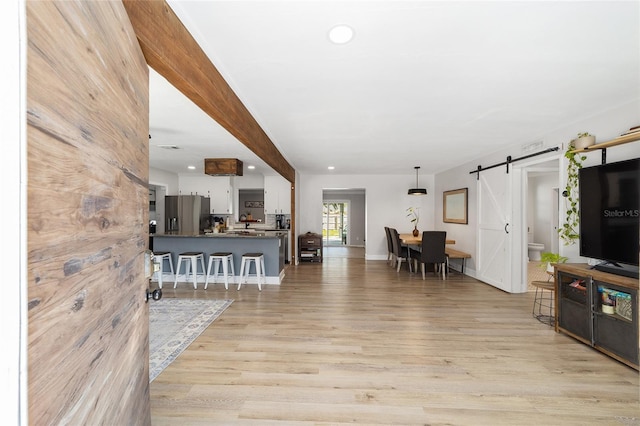 living area featuring baseboards, a barn door, recessed lighting, and light wood-style floors