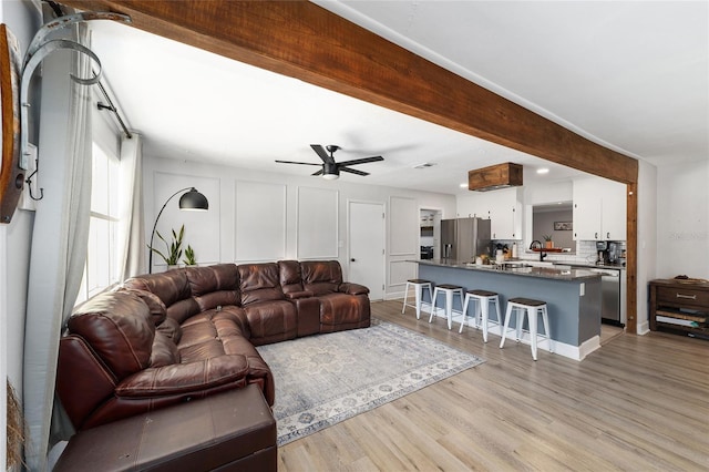 living area featuring beamed ceiling, light wood-style flooring, and ceiling fan