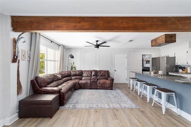 living room featuring beam ceiling, baseboards, ceiling fan, and light wood finished floors