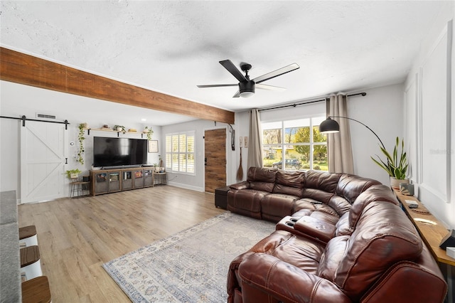 living area featuring a barn door, ceiling fan, a textured ceiling, wood finished floors, and beamed ceiling