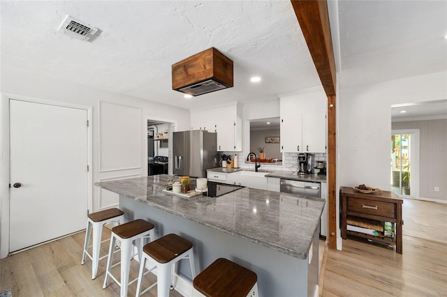 kitchen featuring stainless steel appliances, visible vents, white cabinets, light wood-type flooring, and decorative backsplash