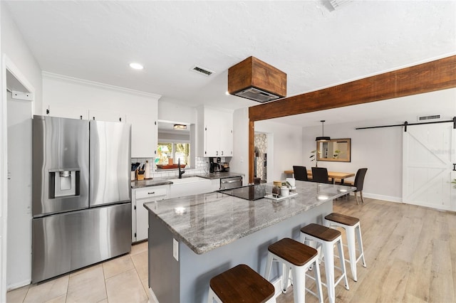 kitchen featuring a barn door, a breakfast bar, white cabinetry, visible vents, and stainless steel fridge with ice dispenser