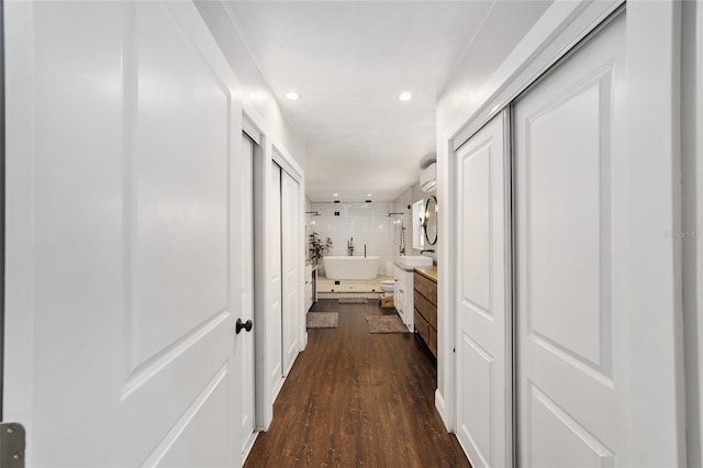 hall with a wall unit AC, dark wood-style floors, a sink, and recessed lighting