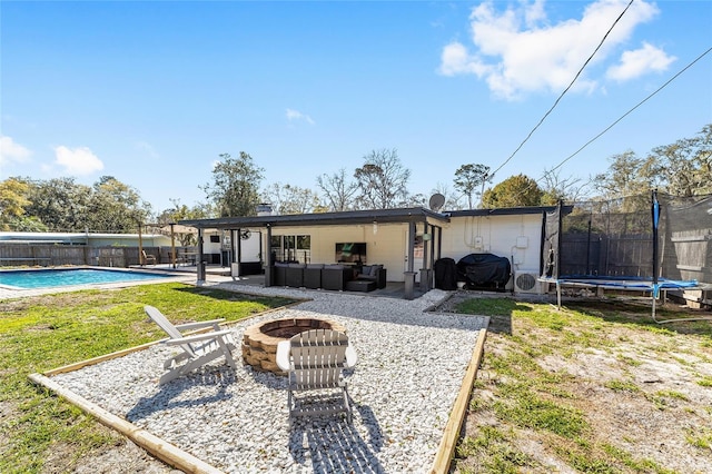 rear view of property featuring a patio, fence, a fenced in pool, a trampoline, and an outdoor living space with a fire pit