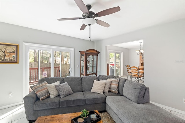 tiled living area with baseboards and ceiling fan with notable chandelier