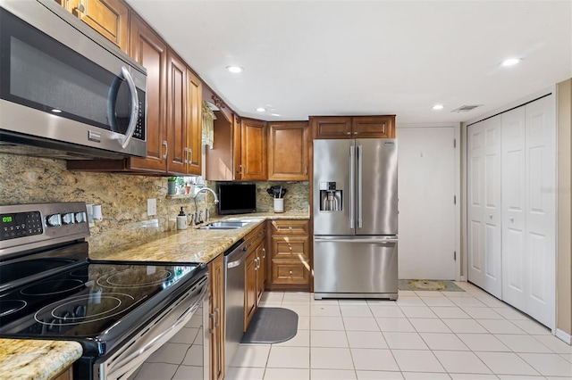 kitchen featuring light stone counters, decorative backsplash, appliances with stainless steel finishes, brown cabinetry, and a sink