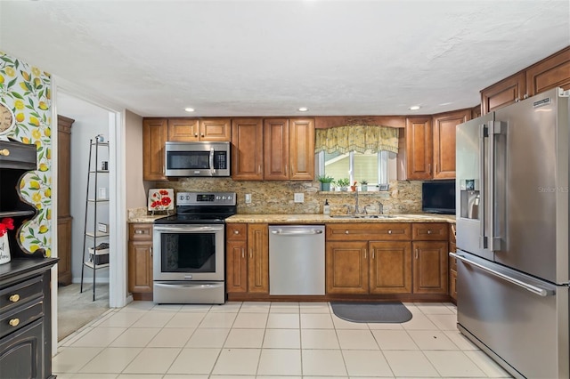 kitchen with brown cabinets, stainless steel appliances, backsplash, a sink, and light stone countertops