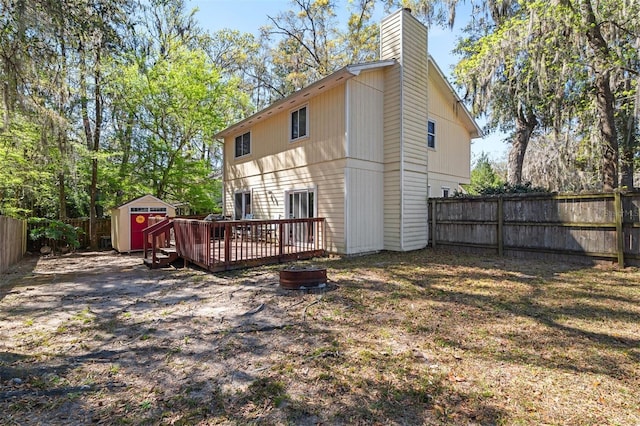 back of property featuring a fenced backyard, a chimney, a storage unit, a wooden deck, and an outdoor structure