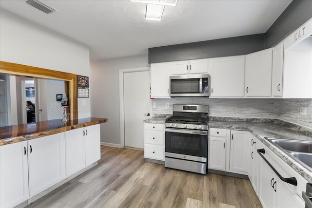 kitchen with stainless steel appliances, backsplash, white cabinets, and light wood-style floors