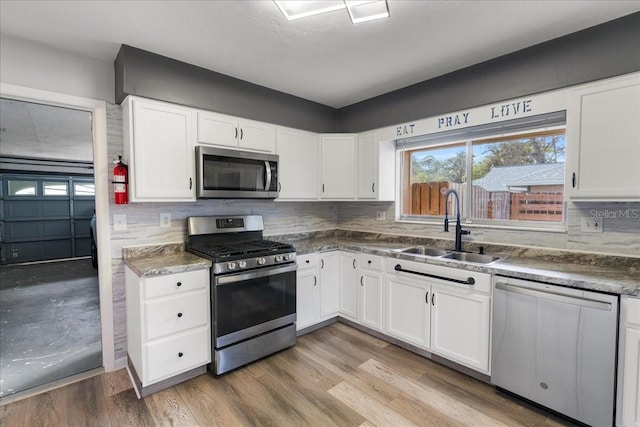 kitchen featuring stainless steel appliances, a sink, white cabinetry, and light wood-style floors