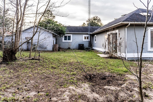 back of house featuring central AC unit, a lawn, and stucco siding