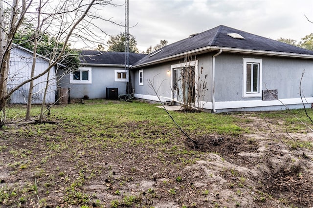 back of property featuring stucco siding, a yard, and central air condition unit