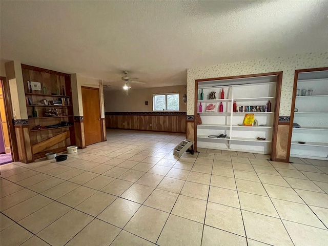 interior space featuring light tile patterned flooring, wainscoting, a textured ceiling, and wallpapered walls