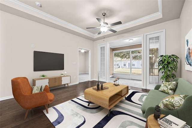 living area featuring ceiling fan, wood finished floors, baseboards, ornamental molding, and a raised ceiling