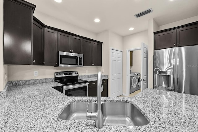 kitchen with visible vents, appliances with stainless steel finishes, light stone counters, and washer and dryer