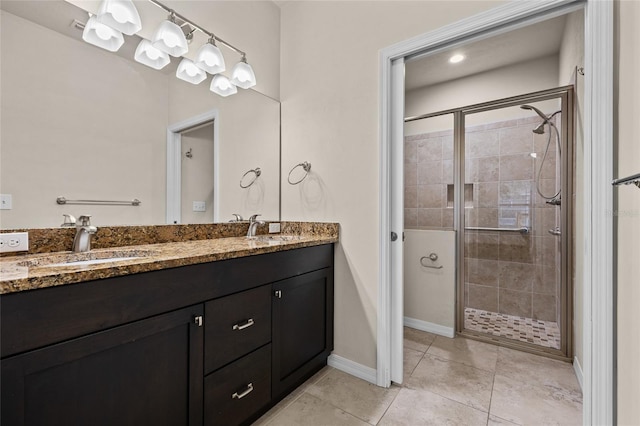 bathroom with double vanity, a sink, a shower stall, tile patterned flooring, and baseboards