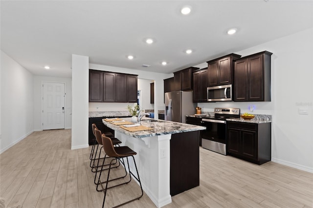 kitchen with dark brown cabinetry, stainless steel appliances, a kitchen breakfast bar, light wood-type flooring, and a center island with sink