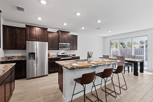 kitchen featuring stone counters, visible vents, stainless steel appliances, and a breakfast bar area