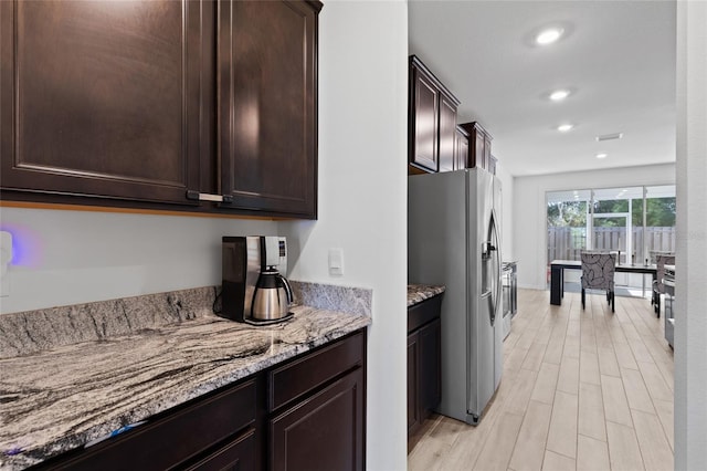 kitchen featuring recessed lighting, stainless steel fridge with ice dispenser, dark brown cabinets, light stone countertops, and light wood finished floors