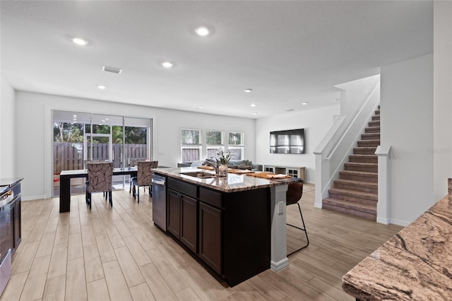 kitchen with visible vents, a breakfast bar area, light stone counters, light wood-type flooring, and a sink