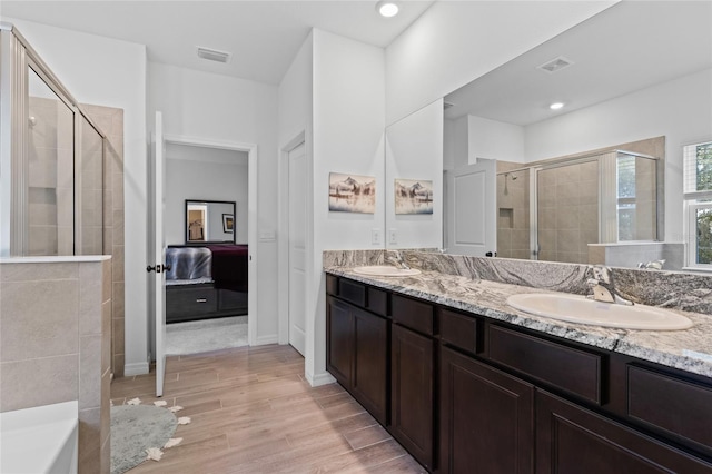 ensuite bathroom with a shower stall, visible vents, a sink, and wood finished floors