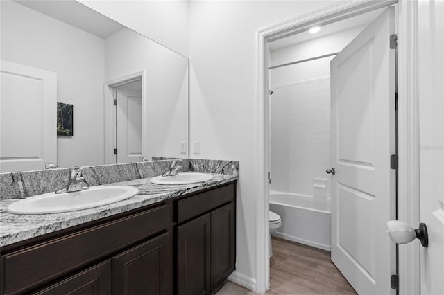 bathroom featuring wood finished floors, a sink, toilet, and double vanity