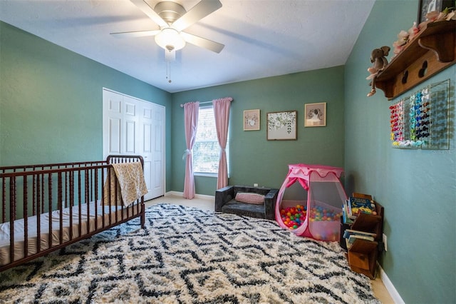 bedroom featuring a ceiling fan, a nursery area, carpet floors, a closet, and baseboards