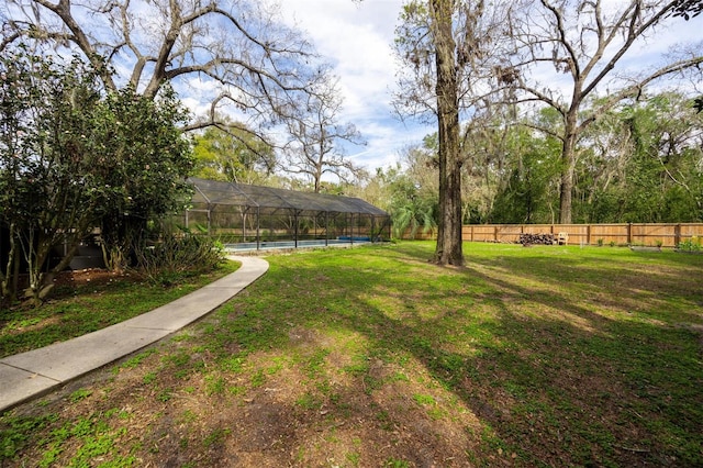view of yard featuring fence, a pool, and glass enclosure
