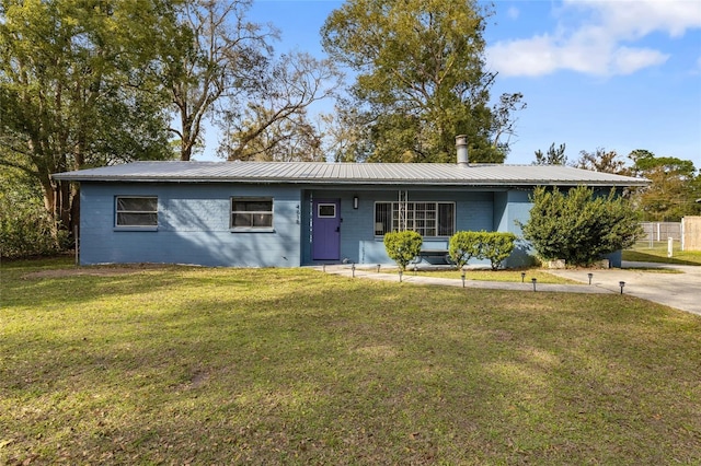 ranch-style house with metal roof, a front yard, and concrete block siding