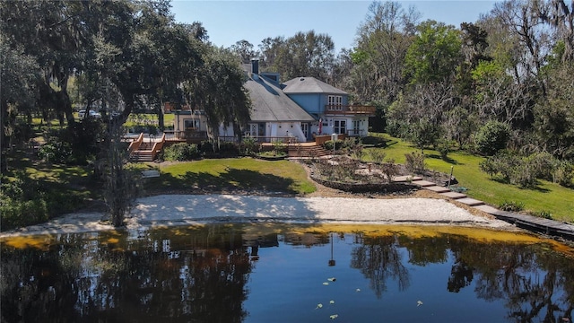 back of house with a chimney, a lawn, and a deck with water view