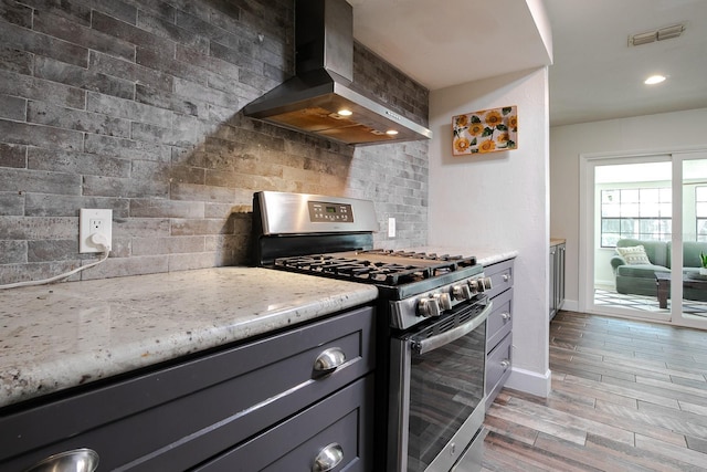 kitchen with visible vents, stainless steel gas stove, gray cabinets, backsplash, and wall chimney exhaust hood