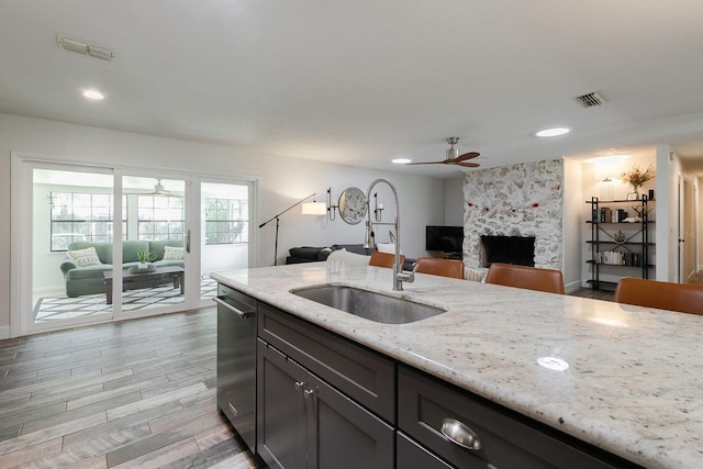 kitchen with light stone counters, a ceiling fan, visible vents, a stone fireplace, and stainless steel dishwasher