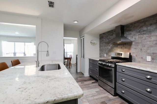 kitchen featuring visible vents, a sink, gas stove, wall chimney range hood, and light stone countertops