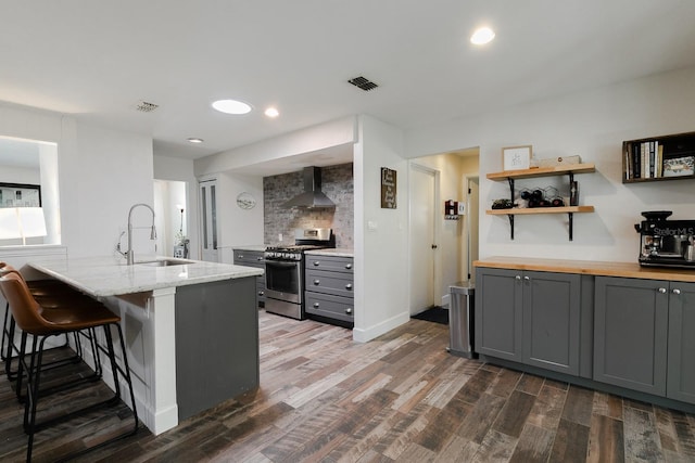 kitchen featuring stainless steel gas range oven, gray cabinetry, a sink, and wall chimney range hood