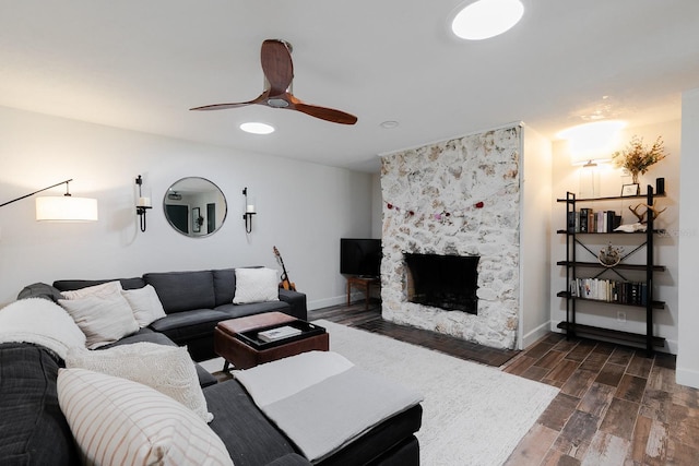 living area featuring wood finish floors, baseboards, a stone fireplace, and a ceiling fan