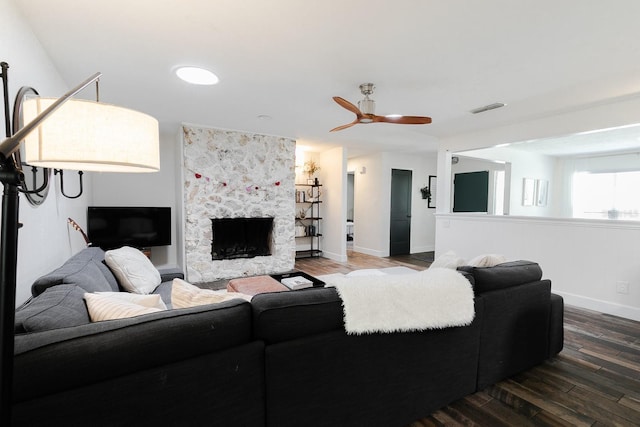 living room with a stone fireplace, baseboards, visible vents, and wood finished floors