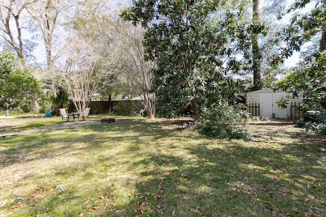 view of yard featuring an outdoor structure, a storage unit, a fenced backyard, and an outdoor fire pit