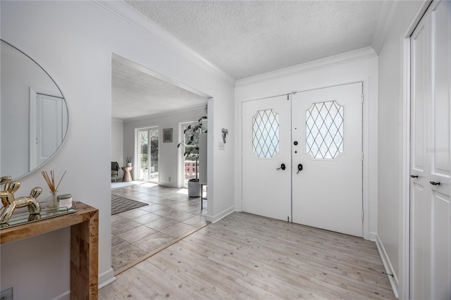 entryway with a textured ceiling, ornamental molding, baseboards, and light wood-style floors